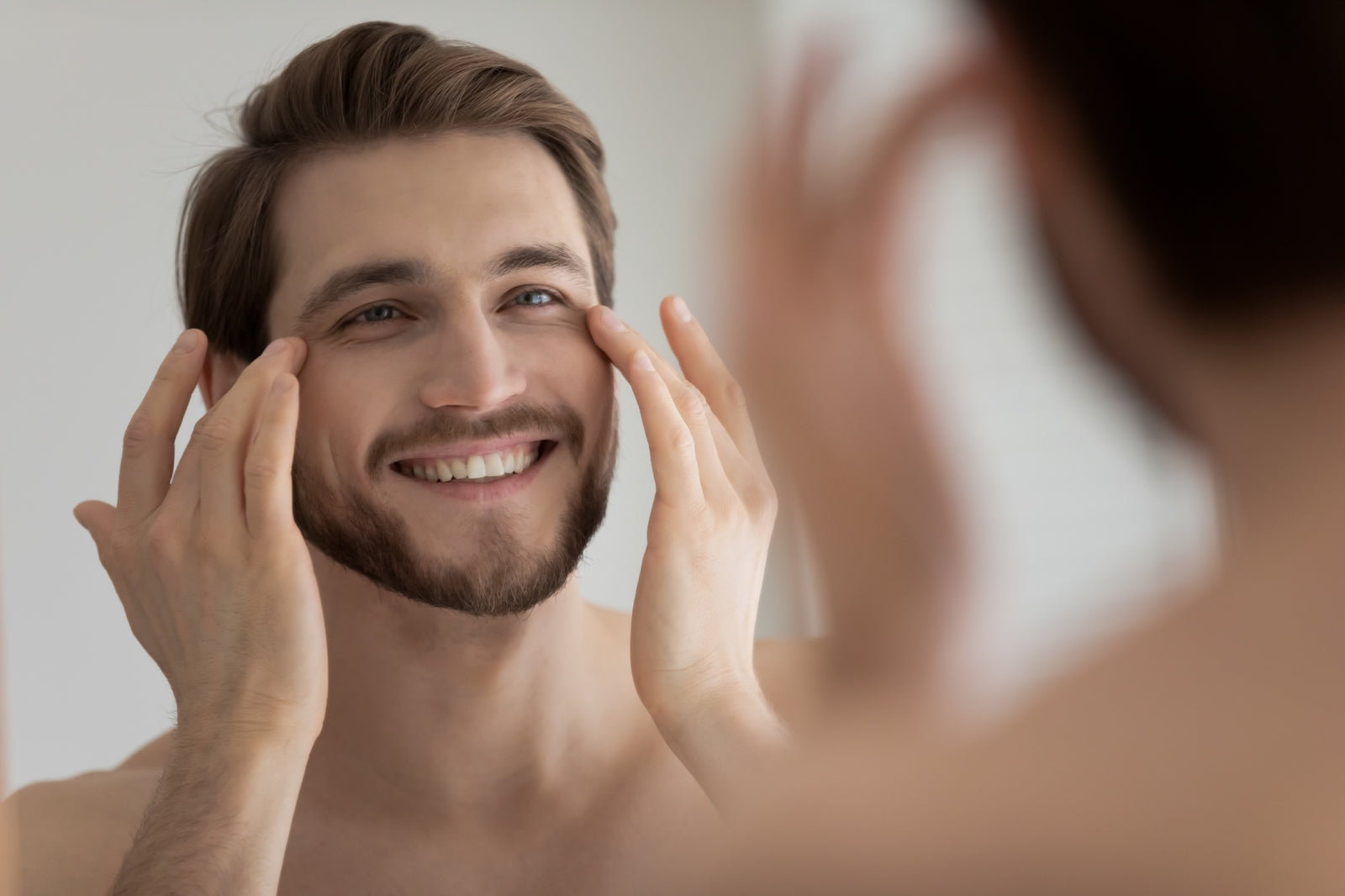 smiling satisfied young man touching skin under eyes